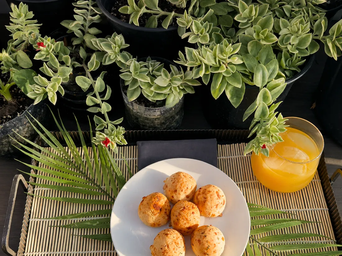 A plate of pão de queijo with a cold drink, served outdoors